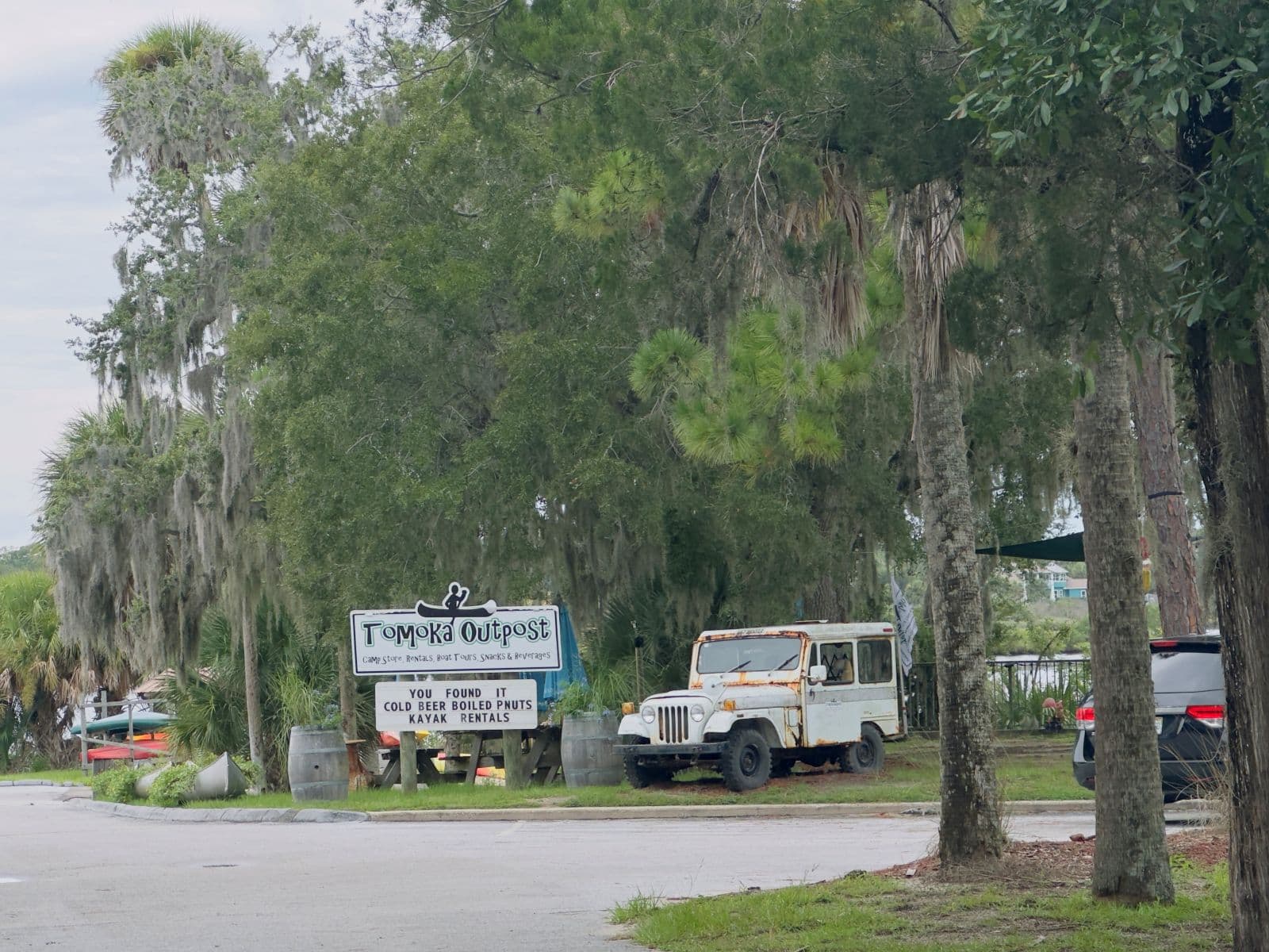 Tomoka Outpost sign, rental canoes, and a vintage Jeep beneath moss-draped trees.